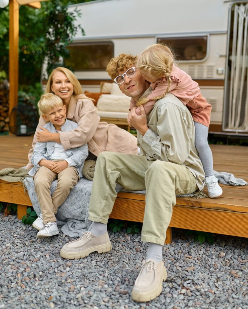 Happy family poses at the trailer, summer camping. Parents with children travel in camp car, nature and forest on background. Campsite adventure, travelling lifestyle