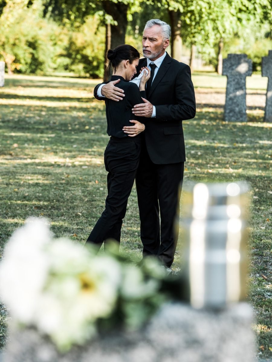 selective focus of senior man hugging upset woman in cemetery